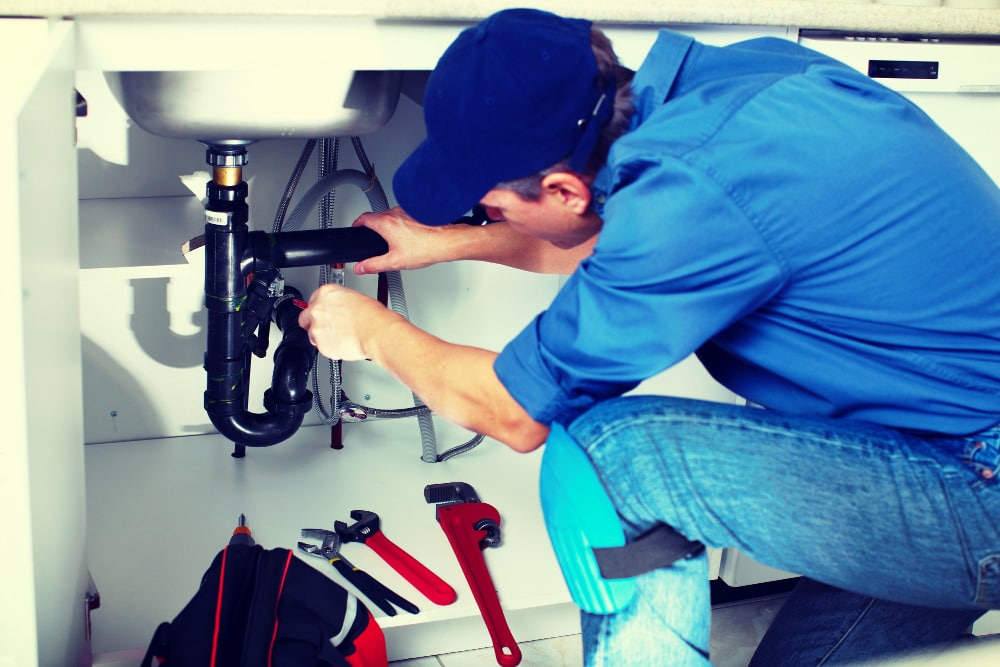 A professional plumber repairing the fixtures beneath a sink.